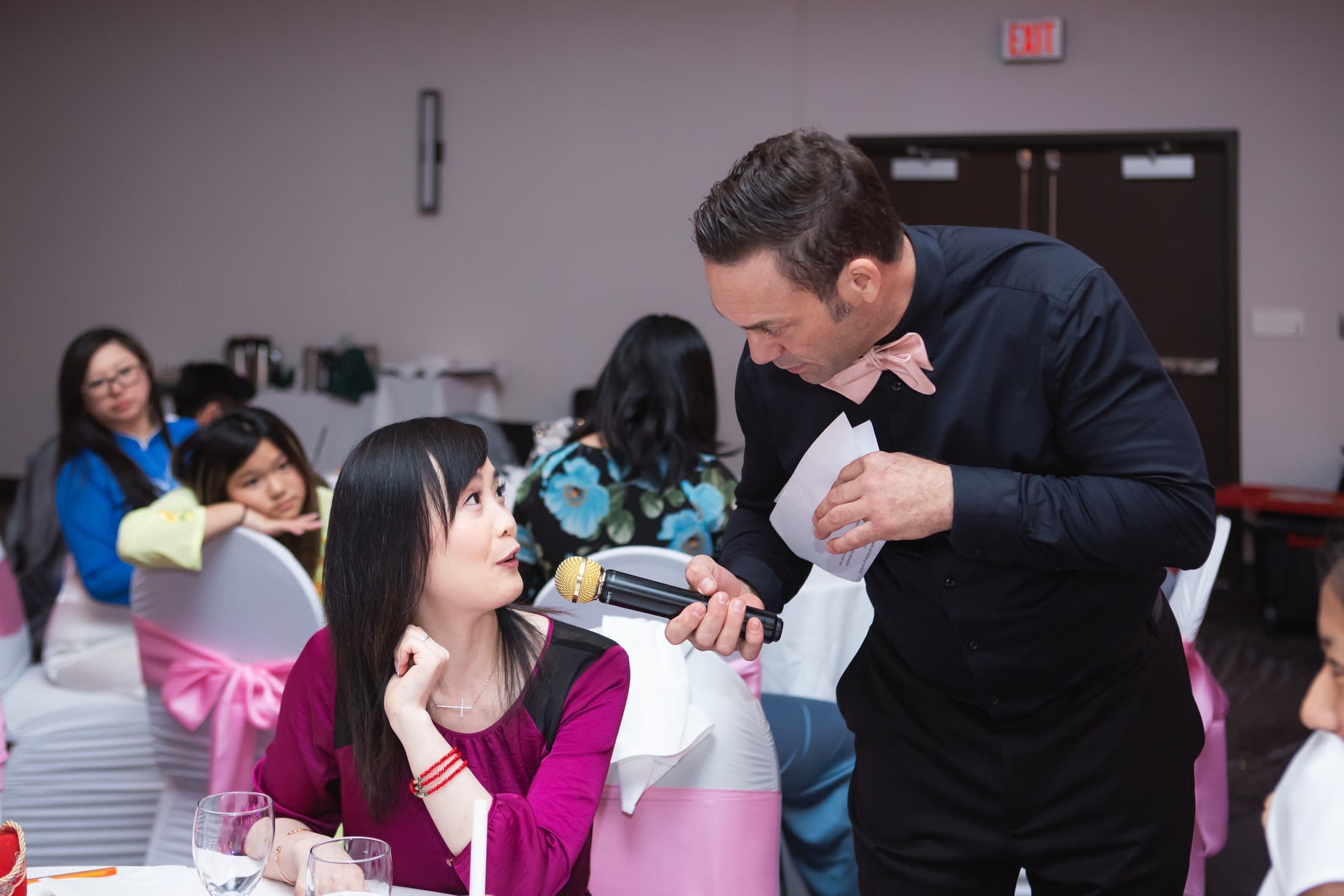 Mike Oulton holding the microphone for a seated guest as her table watches