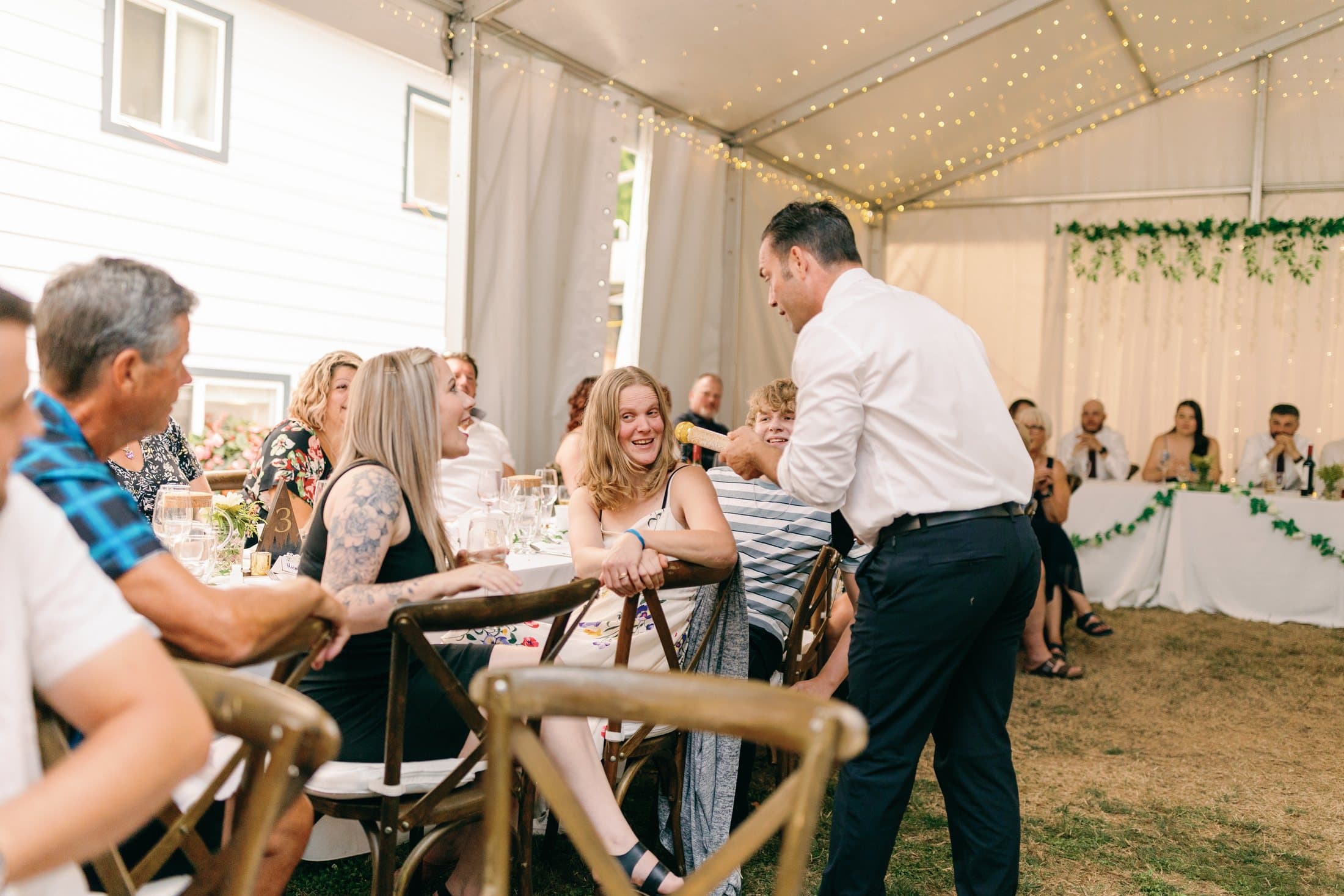 Wedding guests laughing at their table under a marquee as Mike Oulton works the room