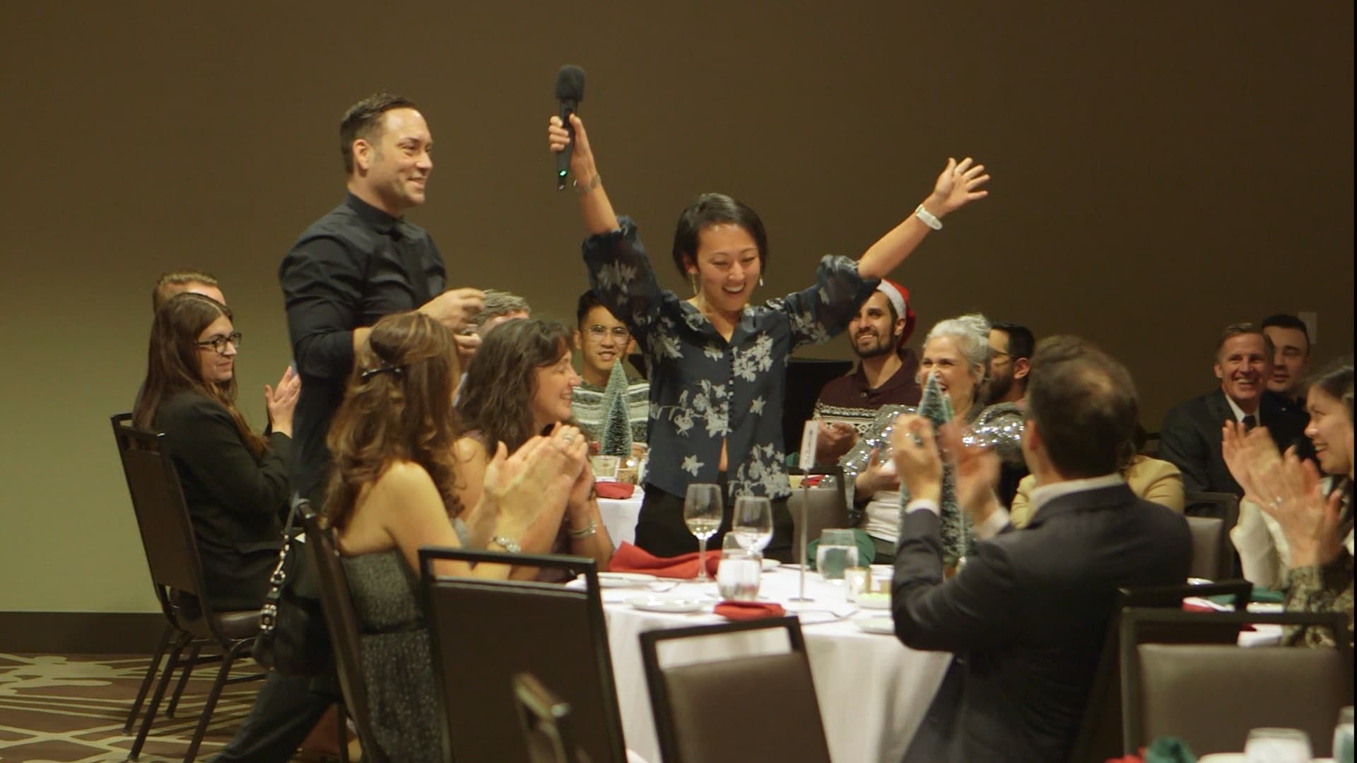 A guest celebrating with both arms up while her table applauds at a Vancouver corporate party
