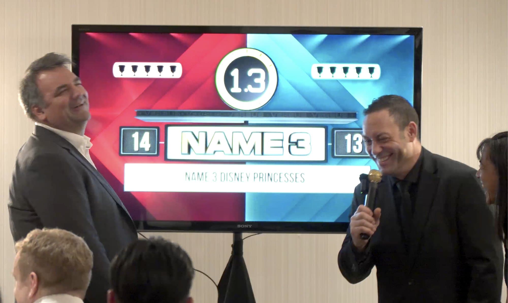 Guests laughing during a custom game show round at a Vancouver event, the scoreboard up on the big screen