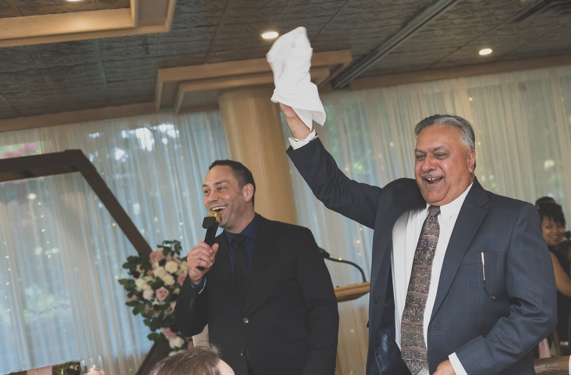 A wedding guest waving his napkin overhead, laughing, as Mike Oulton works the room with the microphone